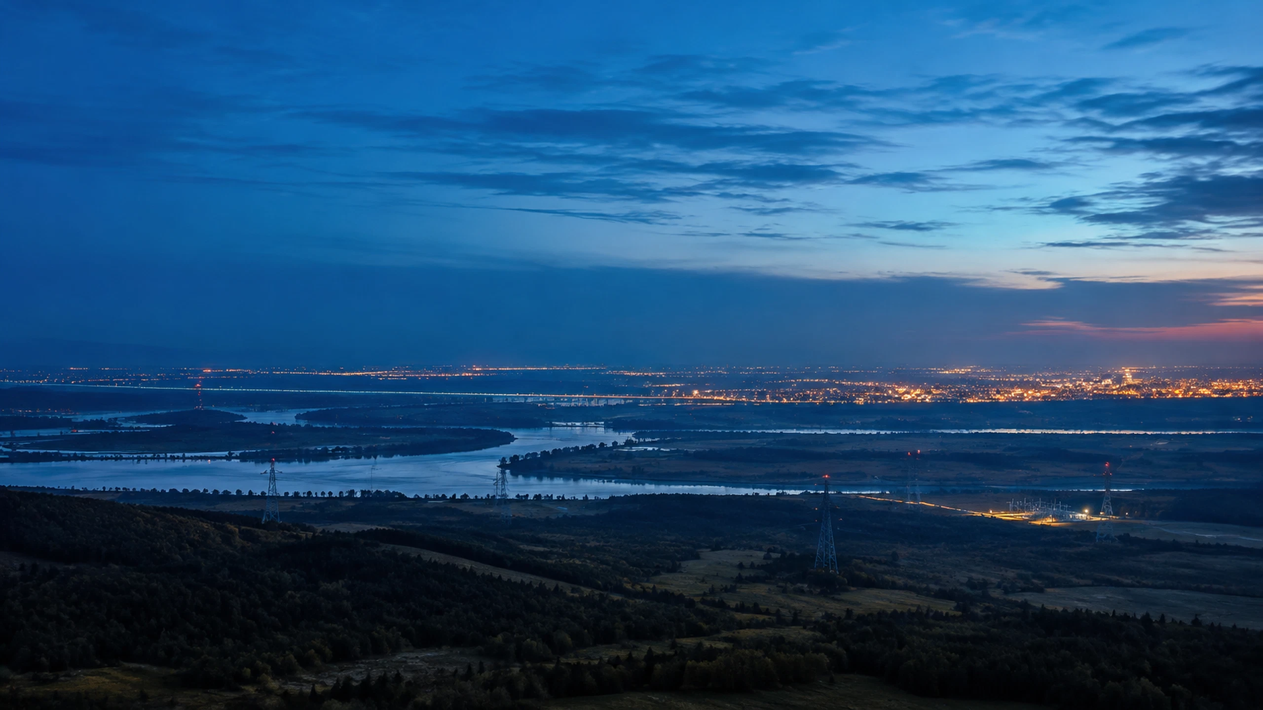 Power infrastructure connecting a river landscape and distant city